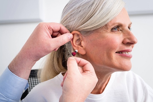 Seniorin bekommt ein modernes Hörgerät von einem Hörakustiker ins Ohr eingesetzt.